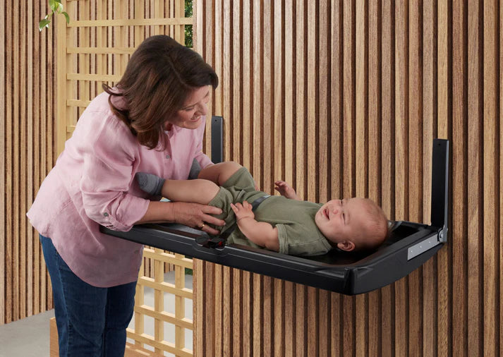 Woman adjusting a baby on a changing table against a wooden wall.