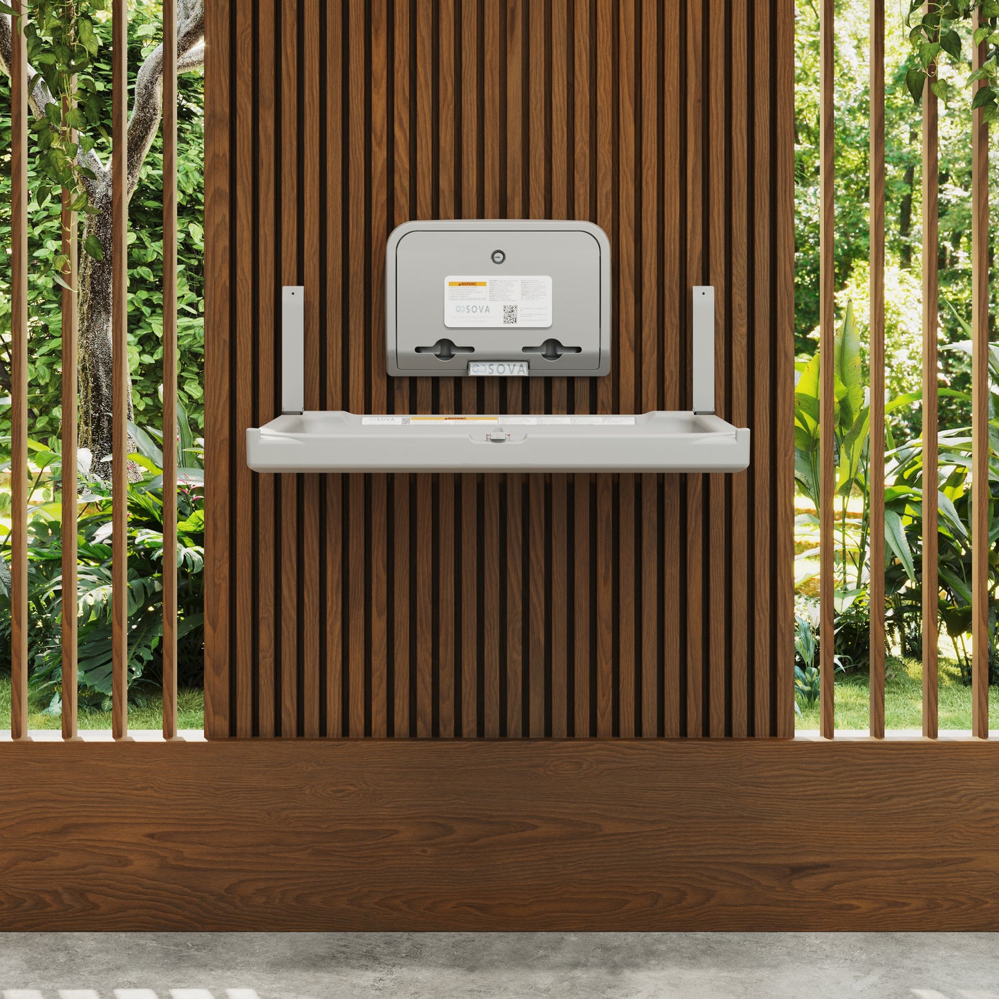 Wall-mounted Gray Element Baby Changing Station with Liner Dispenser against a wooden slatted wall with greenery in the background
