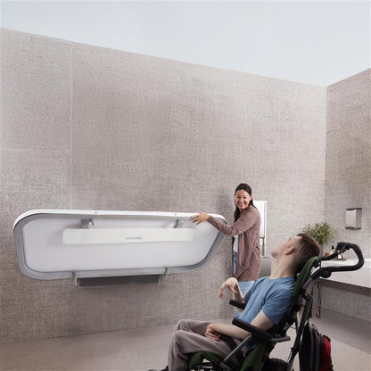 Person using a wheelchair interacting with Attend Adult Changing table in a minimalistic room.