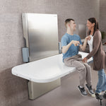 Two people sitting on a modern white adult changing table in a bathroom setting.