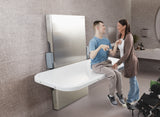 Two people sitting on a modern white adult changing table in a bathroom setting.