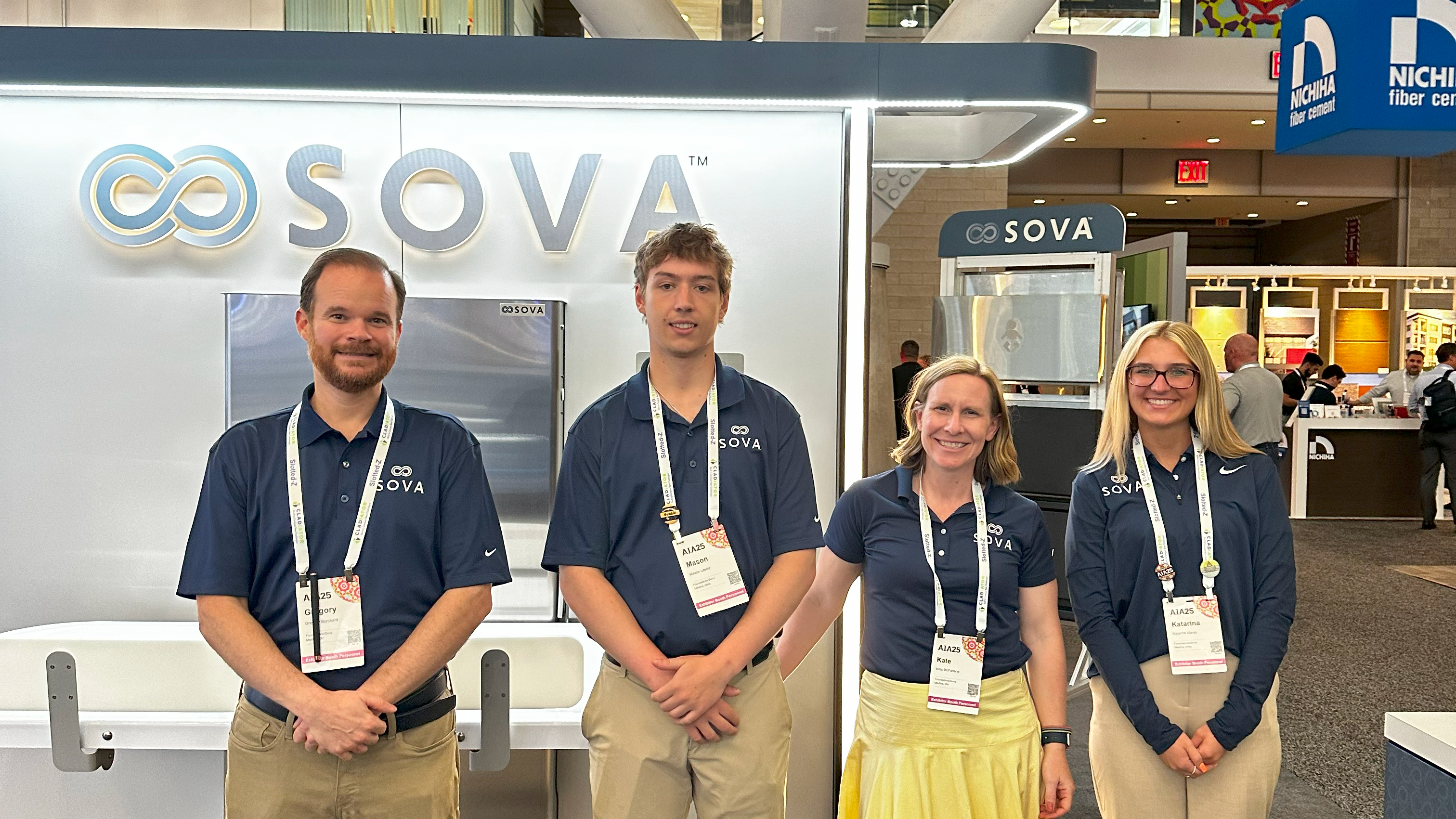 Four individuals in matching navy blue polo shirts with 'SOVA' branding standing in front of a SOVA display.
