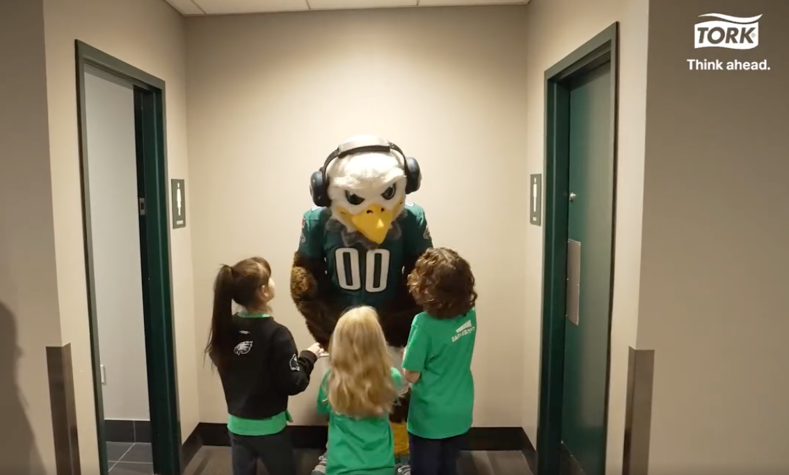 Philadelphia Eagles mascot with kids outside an inclusive restroom featuring an Ascent adult changing table