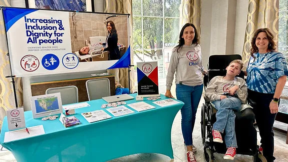 Two women and a child in a wheelchair standing next to a table with inclusion-themed materials.